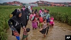 FILE - Rohingya Muslims, who crossed over from Myanmar into Bangladesh, wade past a waterlogged path leading to the Jamtoli refugee camp in Ukhiya, Bangladesh, Nov. 17, 2017. 