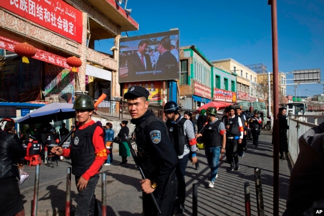 FILE - In this Nov. 3, 2017, photo, armed civilians patrol the area outside the Hotan Bazaar where a screen shows Chinese President Xi Jinping in Hotan, in western China's Xinjiang region. Acting Deputy Assistant Secretary of State Laura Stone said April 18, 2018, that the United States was deeply concerned about China's detention of at least "tens of thousands" of ethnic Uighurs and other Muslims and could take action under the Global Magnitsky Act.
