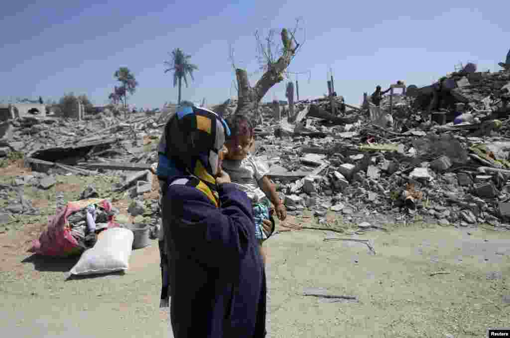A Palestinian woman holds her daughter as they walk past the ruins of destroyed houses in Khuzaa town, which witnesses say was heavily hit by Israeli shelling and air strikes during the Israeli offensive, in the east of Khan Younis, in the southern Gaza Strip, Aug. 7, 2014.