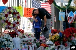 FILE - Gary Mendoza, and his son Michael pay their respects at a makeshift memorial site honoring shooting victims, in San Bernardino, Calif., Dec. 7, 2015.