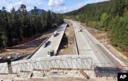 In this photo taken Oct. 4, 2018, Interstate 90 traffic passes under a wildlife bridge under construction on Snoqualmie Pass, Washington.