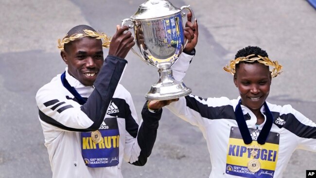 Benson Kipruto, left, and Diana Kipyogei, right, both of Kenya, celebrate at the finish line after winning the men's and women's division of the Boston Marathon in Boston, Oct. 11, 2021.