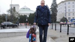 Polish lawmaker Michal Stasinski poses in front of the parliament pulling a suitcase with warm clothes and carrying a bag filled with his mother's homemade cabbage-and-mushroom stuffed dumplings in Warsaw, Poland, Dec. 23, 2016. Stasinski was joining a group of opposition lawmakers hunkering down for sit-in occupation of parliament to protest what they consider backsliding on democracy by the populist government. 