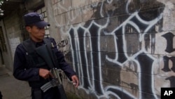 FILE - A member of the Salvadoran National Police walks next to symbol of the Mara Salvatrucha gang painted on a wall during an anti-gang operative in San Salvador, March 7, 2014.