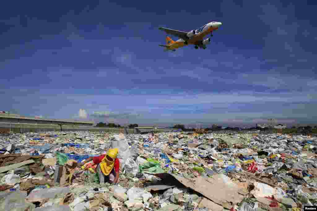 An aircraft flies overhead as a person rummages for recyclables at a garbage dumpsite in Paranaque city, metro Manila, Philippines.