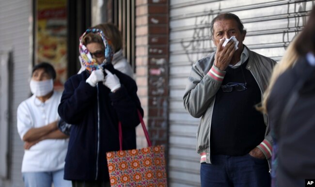 La gente, usando diferentes métodos para taparse la boca y la nariz, hacen cola frente a un banco en Buenos Aires, Argentina, el 4 de abril de 2020.