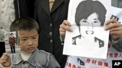 A young boy holds up a photo of his mother as he joins family members wearing posters describing the woman as missing from her home in Xian, northern China's Shaanxi province, as they launch a campaign to locate her (File Photo).