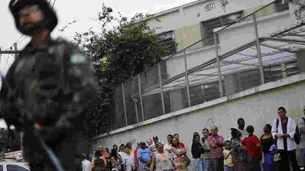 A soldier stands guard where people wait in line to vote in general elections outside a school at the Mare Complex slum in Rio de Janeiro, Brazil, Oct. 26, 2014. 