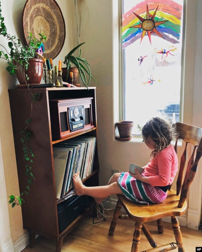 In this April 2, 2020, photo provided by Cassy Quinlan, 4-year-old Polly Fraley listens in Homer, Alaska, to children's stories being read on air at local radio station KBBI by librarian Claudia Haines.