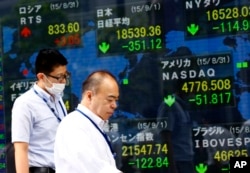 Men walk past an electronic stock indicator of a securities firm in Tokyo, Sept. 1, 2015.