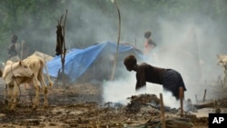 A young South Sudanese woman scrubs the dung-covered ground in preparation for cows to return from grazing, at a cattle camp outside the town of Rumbek, South Sudan, July 31, 2017.