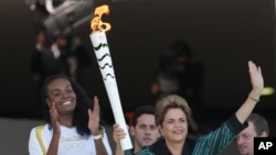 FILE - Brazil’s now-suspended President Dilma Rousseff holds the Olympic flame next to athlete Fabiana Claudino in Brasilia, Brazil, May 3, 2016.