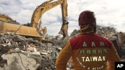 FILE - A member of rescue teams stands by as heavy excavation machinery continues to dig through the rubble of a collapsed building complex in Tainan, Taiwan, Thursday, Feb. 11, 2016.