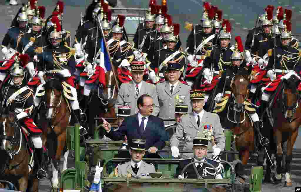 French President Francois Hollande, standing left in the command car, drives down the Champs-Elysees during the Bastille Day parade in Paris, France, July 14, 2014.