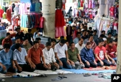 Muslim men perform Friday prayer amid clothing displayed at fashion stalls in Tanah Abang market in Jakarta, Indonesia, Friday, June 2, 2017