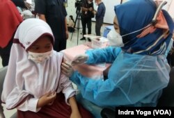 Seorang siswi SD Negeri Cempaka Putih Timur 03 sedang disuntik vaksin Covid-19 dari Sinovac saat program vaksinasi untuk anak usia 6 hingga 11 tahun dimulai pada 14 Desember 2021 ini. (VOA/Indra Yoga)