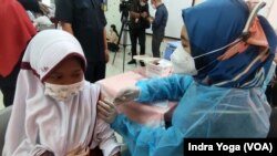 Seorang siswi SD Negeri Cempaka Putih Timur 03 sedang disuntik vaksin Covid-19 dari Sinovac saat program vaksinasi untuk anak usia 6 hingga 11 tahun dimulai pada 14 Desember 2021 ini. (VOA/Indra Yoga)