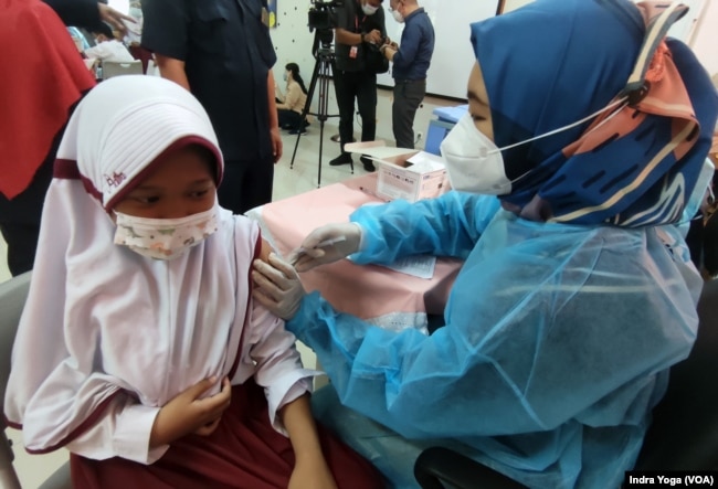 Seorang siswi SD Negeri Cempaka Putih Timur 03 sedang disuntik vaksin Covid-19 dari Sinovac saat program vaksinasi untuk anak usia 6 hingga 11 tahun dimulai pada 14 Desember 2021 ini. (VOA/Indra Yoga)
