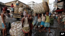 Indian laborers carry a giant basket of vegetables to a wholesale market in Kolkata, India, Aug. 21, 2013. 