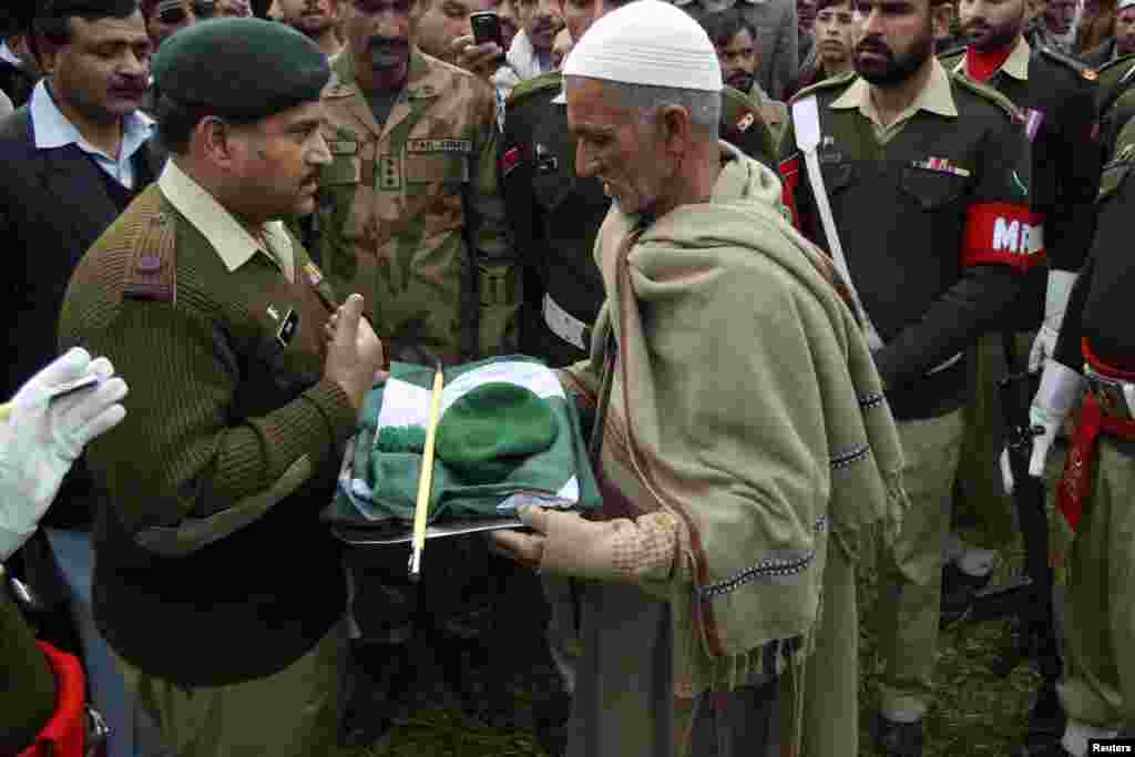 A military official hands over a Pakistan military cap, stick and national flag to the father of Pakistani soldier Muhammad Akhlaq, after his burial at his village Pind Bainso, Tehsil Kallar Saydan, Rawalpindi. The military said he was killed by Indian soldiers while crossing into the Indian side of Kashmir at a post in Khoi Ratta sector on the Line of Control in the disputed region of Kashmir.