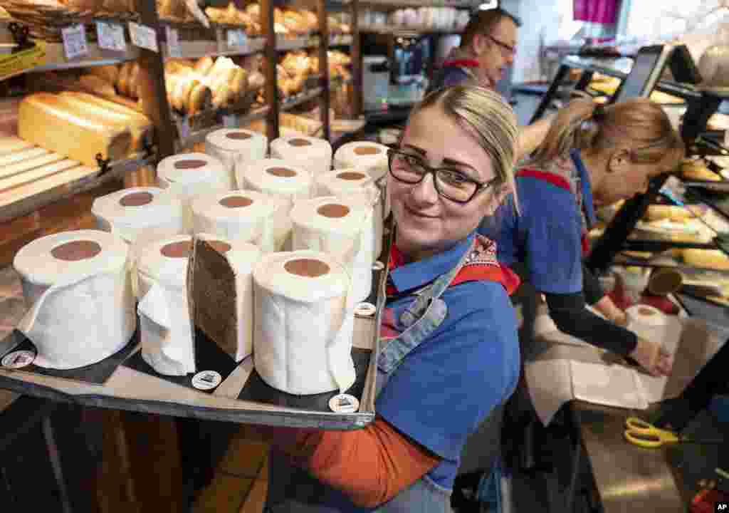 A saleswoman of the bakery Schuerener Backparadies shows a tray with round marble cakes wrapped in fondant that look like toilet paper rolls in Dortmund, Germany.