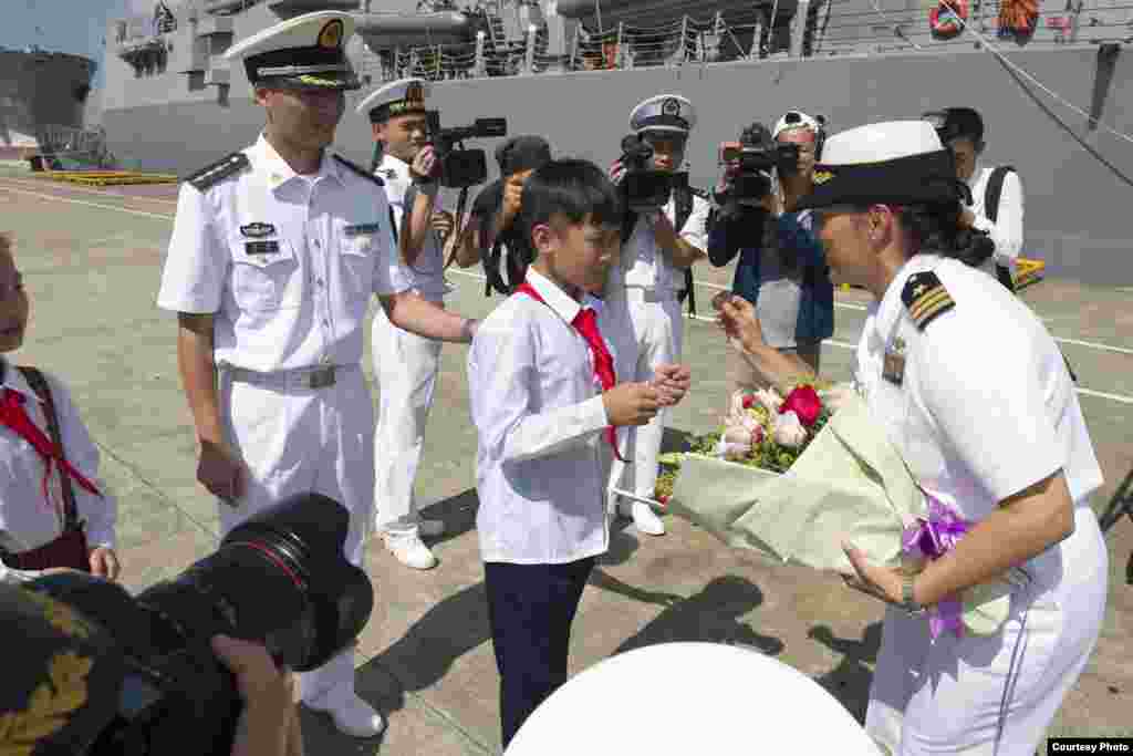 美軍斯泰雷特號導彈驅逐艦2017年6月12日抵達中國湛江港時女艦長卡洛里從中國少年手裡接過鮮花後，展示該軍艦的紀念性硬幣（美國海軍照片）。這是川普行政當局年初上任以來兩國海軍之間首次進行艦艇互訪，這標誌著美中兩國恢復了擱置幾個月之久的海軍互訪項目。