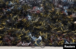 A worker rides a shared bicycle past piled-up shared bikes at a vacant lot in Xiamen, Fujian province, China.