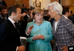 French President Emmanuel Macron, left, speaks with German Chancellor Angela Merkel, center, and Managing Director of the International Monetary Fund Christine Lagarde, right, as they attend a round table meeting of G7 leaders in Taormina, Italy, May 27,