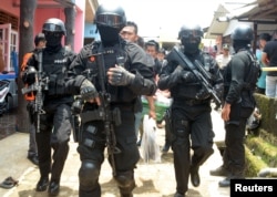 FILE - Armed anti-terror police walk ahead of guard officers carrying bags of evidence from the house of a man suspected of being involved in Islamic State-related activities in south Tangerang, Indonesia's Banten province, in March 2015.