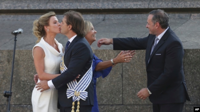 El nuevo presidente de Uruguay, Luis Lacalle Pou, y su esposa Lorena Ponce de León se besan, a la izquierda, mientras la vicepresidenta Beatriz Argimon, segunda a la derecha, es abrazada por el líder del Partido Nacional, Alvaro Delgado, después de prestar juramento en Montevideo, Uruguay, el domingo 1 de marzo de 2020.