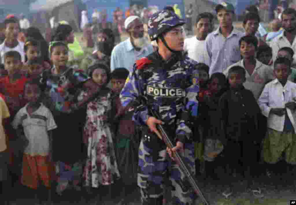 An armed police officer guards as Muslim refugees stand behind him at Sittwe, Myanmar 