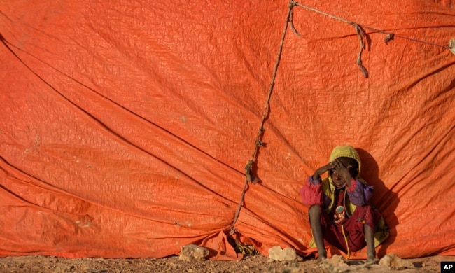 A young Somali boy sits outside his makeshift hut at a camp for people displaced from their homes elsewhere in the country by the drought, shortly after dawn in Qardho, Somalia, March 9, 2017.