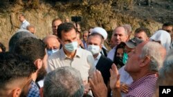In this photo released Tuesday, Oct. 13, 2020 on the official Facebook page of the Syrian Presidency, Syrian President Bashar Assad, center, wearing a mask to help prevent the spread of the coronavirus, speaks with people during his visit to the coastal province of Latakia, Syria