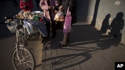 A woman, right, pays money to a street vendor, center, for a bag of apple she bought near the vendor's tricycle cart in Beijing, China, 11 Dec 2010