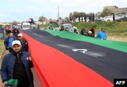 Libyans carry a giant national flag in the capital Tripoli during a celebration to mark the the upcoming eighth anniversary of the Libyan revolution that toppled Moammar Gadhafi, Feb. 25, 2019.