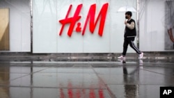 A man carrying an umbrellas walks past an H&M clothing store at a shopping mall in Beijing, Friday, March 26, 2021. H&M disappeared from the internet in China as the government raised pressure on shoe and clothing brands. (AP Photo/Mark Schiefelbein)