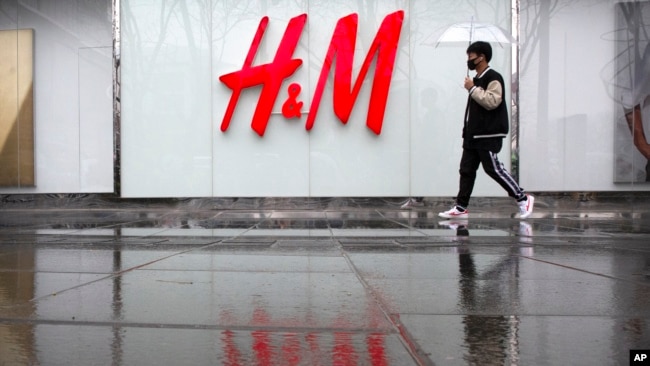 A man carrying an umbrellas walks past an H&M clothing store at a shopping mall in Beijing, Friday, March 26, 2021. H&M disappeared from the internet in China as the government raised pressure on shoe and clothing brands. (AP Photo/Mark Schiefelbein)