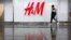 A man carrying an umbrellas walks past an H&M clothing store at a shopping mall in Beijing, Friday, March 26, 2021. H&M disappeared from the internet in China as the government raised pressure on shoe and clothing brands. (AP Photo/Mark Schiefelbein)