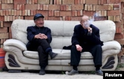 FILE - An elderly man (R) smokes a pipe as he chats with another man on a sofa in front of piles of bricks in Yongji, Shanxi province, China. In China, the government’s policy is to have 90 percent of old age care in the home, seven percent at the community level and just three percent in retirement homes.