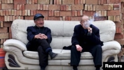 陕西省永济县两位退休老人在一座砖堆前的沙发上抽烟聊天。