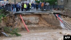 Warga berkerumun di dekat jalanan yang rusak tersapu oleh banjir di Villegailhenc, Aude, Perancis, Senin (15/10).