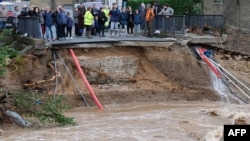 People stand in front of a collapsed road on Oct. 15, 2018 in Villegailhenc in the Aude department after it was particularly badly hit by heavy rain storms which swamped parts of southwestern France, flooding rivers and cutting roads, killing at least six