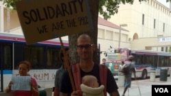 Cristian, un profesor de primaria en la ciudad de Miami, muestra su letrero durante la protesta "Ocupemos Miami".