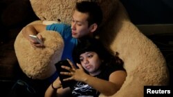 Cory Brandi (L), 25, and Isha Padhye (right), 23, who is a UI engineer, check their phones as they rest together on large stuffed bear at The Negev tech house in San Francisco, California, Feb. 4, 2017. 