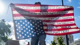Gabriel Black Elk, who is Lakota, kneels on the neck of a fallen statue of Christopher Columbus and holds an American flag with the names of Native Americans killed by police, at the Minnesota state Capitol in St. Paul, Minn., June 10, 2020. (Evan Frost)