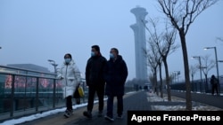 People walk along a path as the Beijing Olympic Tower is seen during a smoggy day in Beijing, Jan. 24, 2022. 