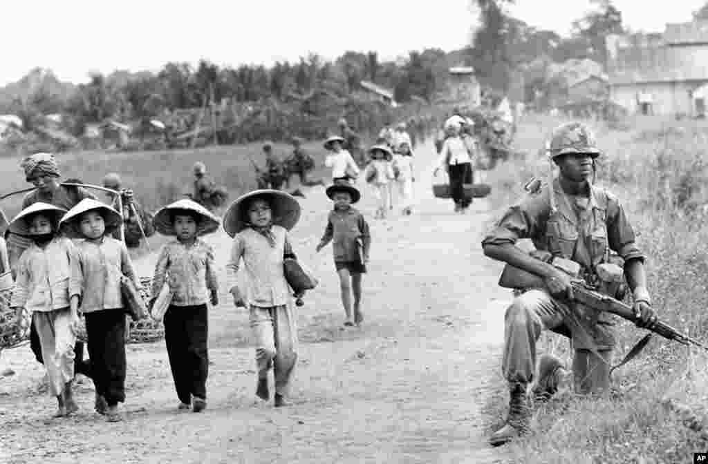 Tháng 12-1965: Một binh sĩ thuộc Sư Đoàn 1 Bộ Binh Hoa Kỳ bảo vệ quốc lộ 7 trong lúc phụ nữ và trẻ em Việt Nam tại Bến Cát trở về nhà. (AP)