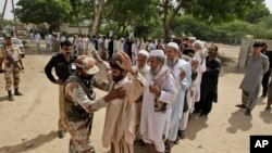 A Pakistani paramilitary soldier checks voters before they enter a polling station to cast their ballots, in Karachi, Pakistan, May 11, 2013.