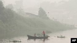 A man rows a boat on Siak River as thick haze from wildfires blanket the city in Pekanbaru, Riau province, Indonesia, Monday, Oct. 5, 2015. The haze covered parts of neighboring Malaysia and Singapore for about a month.