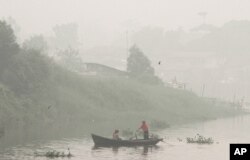 FILE - A man rows a boat on Siak River as thick haze from wildfires blanket the city in Pekanbaru, Riau province, Indonesia, Oct. 5, 2015.